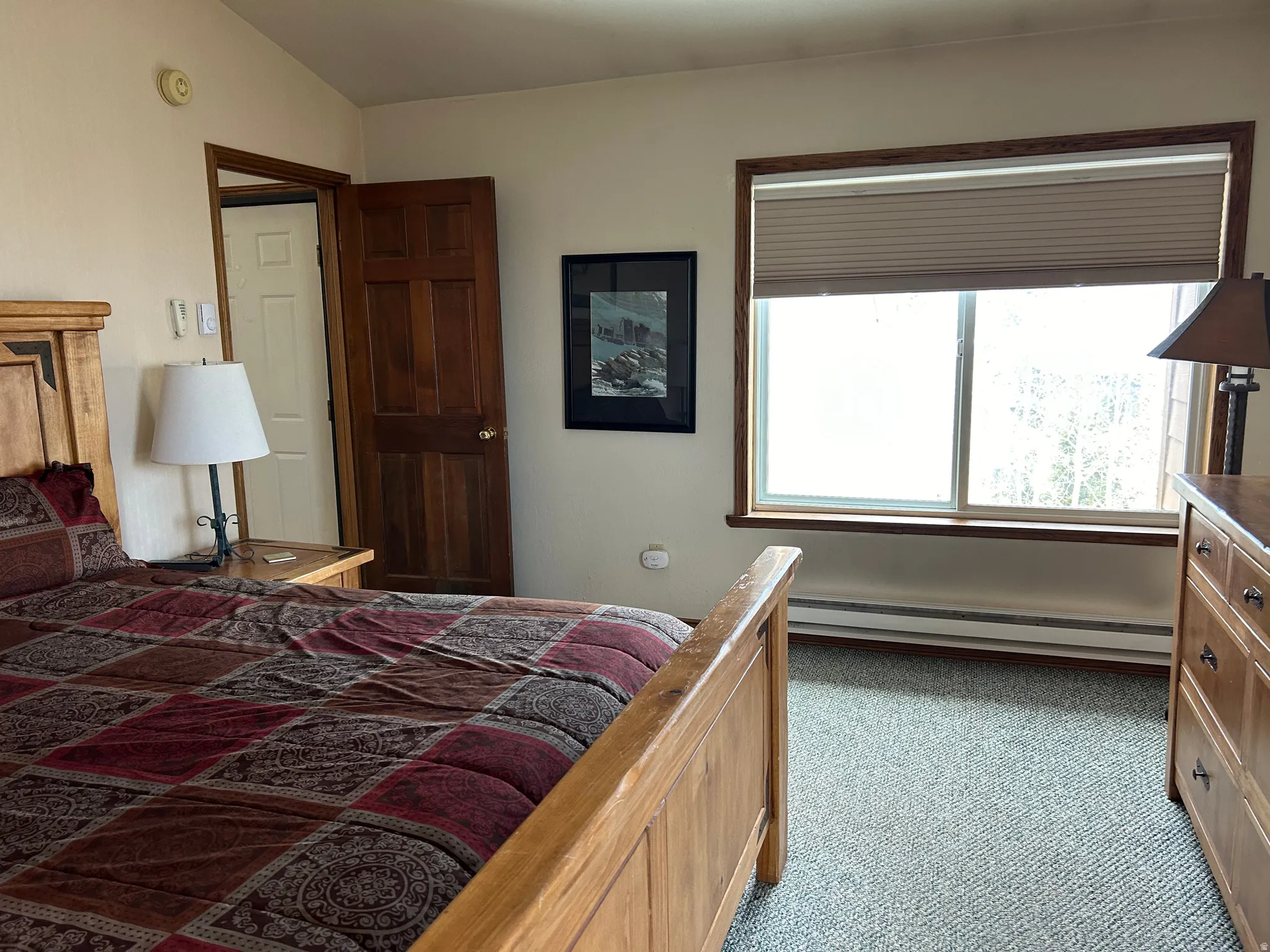 Bedroom featuring a large window with wood trim, cellular shades, and carpeting