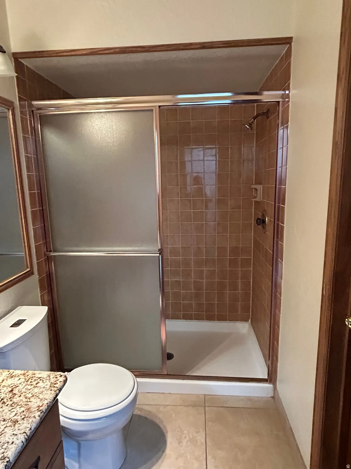 Tiled shower stall with a sliding frosted glass door, featuring a white shower pan and a bronze-finish showerhead