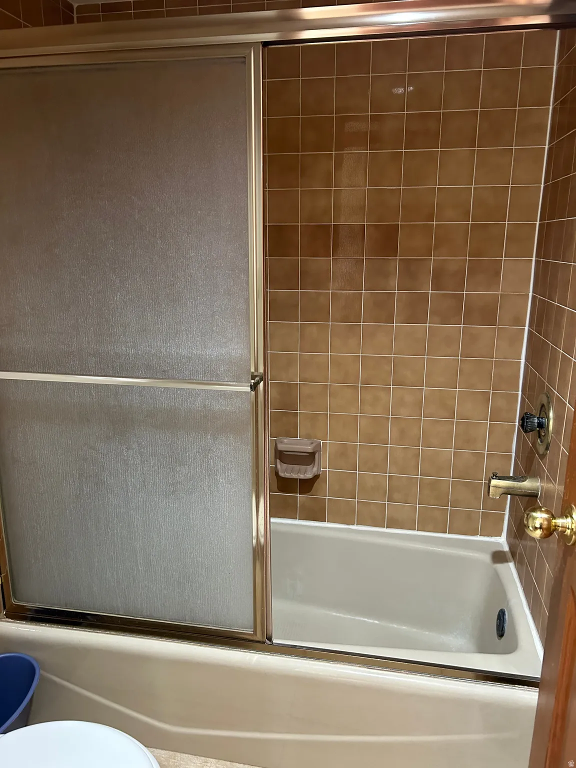Full bathtub with tiled surround and sliding frosted glass shower doors