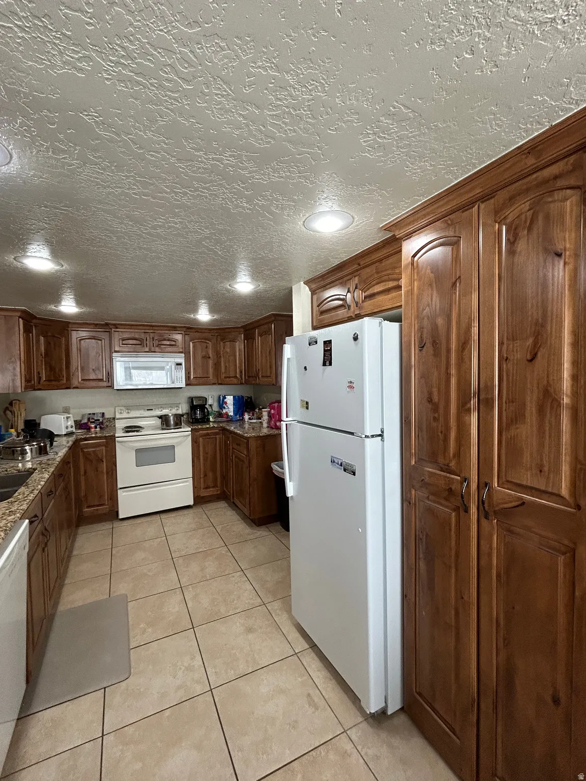 Kitchen featuring extensive wood cabinetry, granite countertops, white appliances, and ceramic tile flooring
