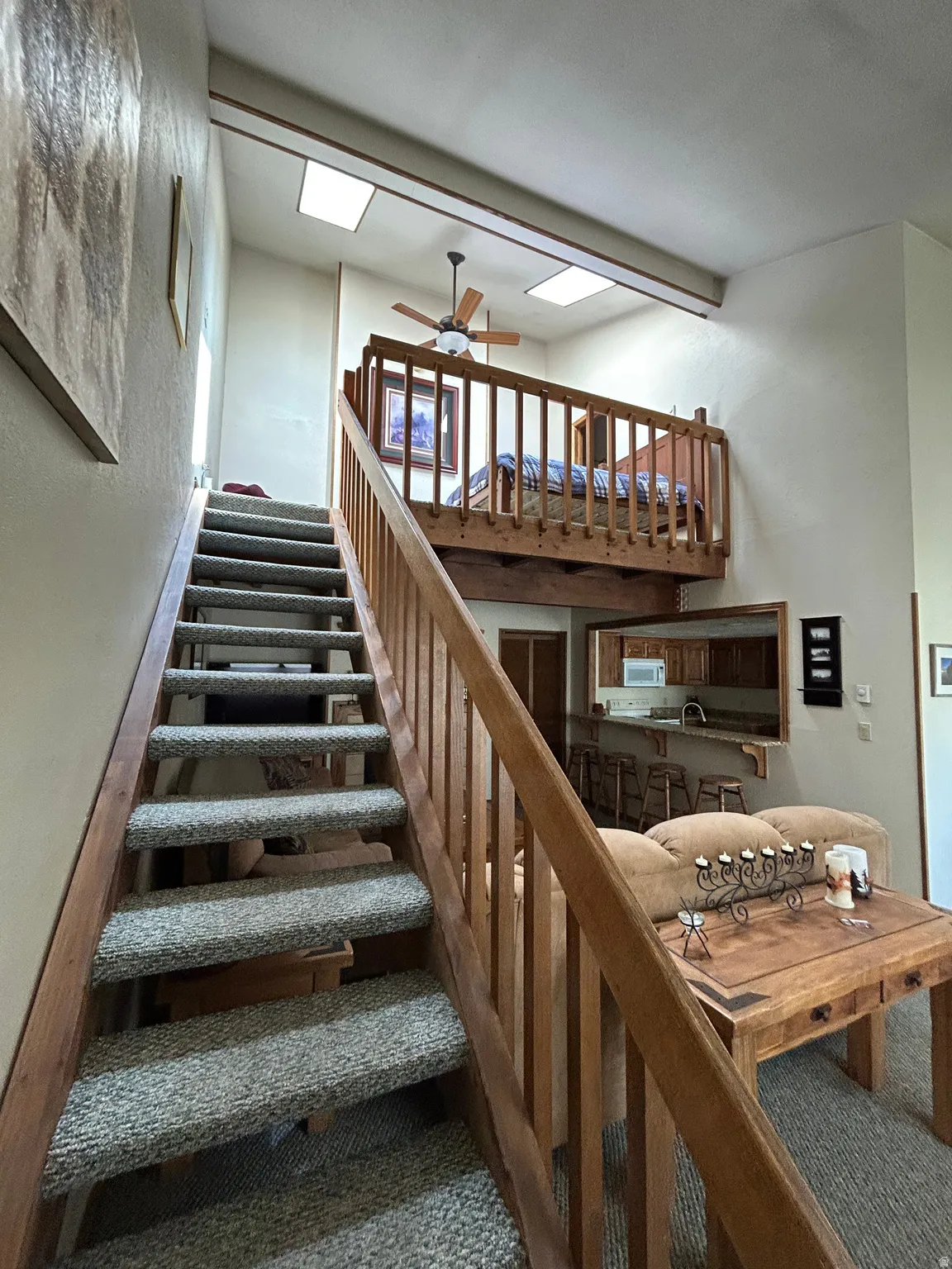 Interior staircase with carpeted treads and wood railings, leading to an upper loft area