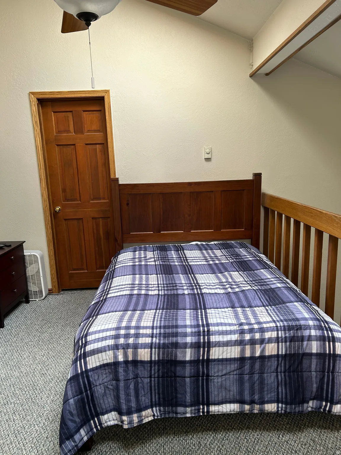 Carpeted bedroom with a natural wood door, wood-finish ceiling fan, and sloped ceiling