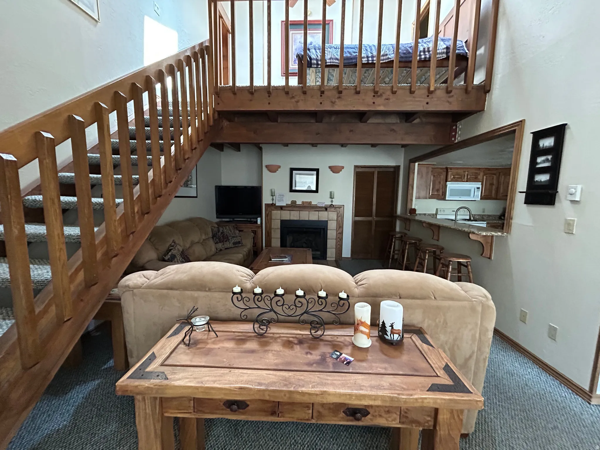 Open-concept living area featuring a wood staircase with carpeted treads, a loft space with a wood railing, and a kitchen pass-through with a breakfast bar