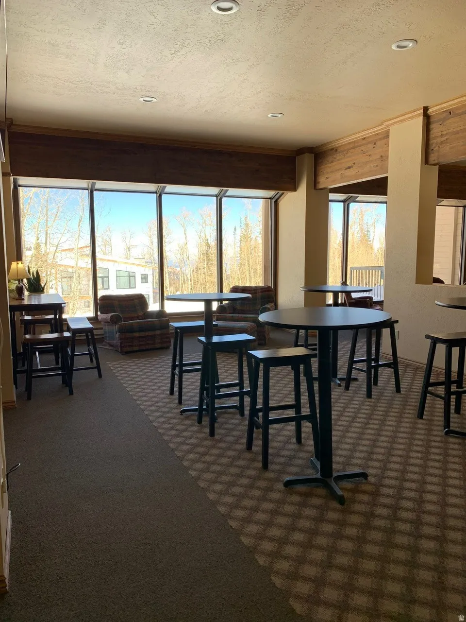 Expansive commercial space featuring large picture windows, recessed lighting, wood-finish ceiling beams, and patterned carpet flooring