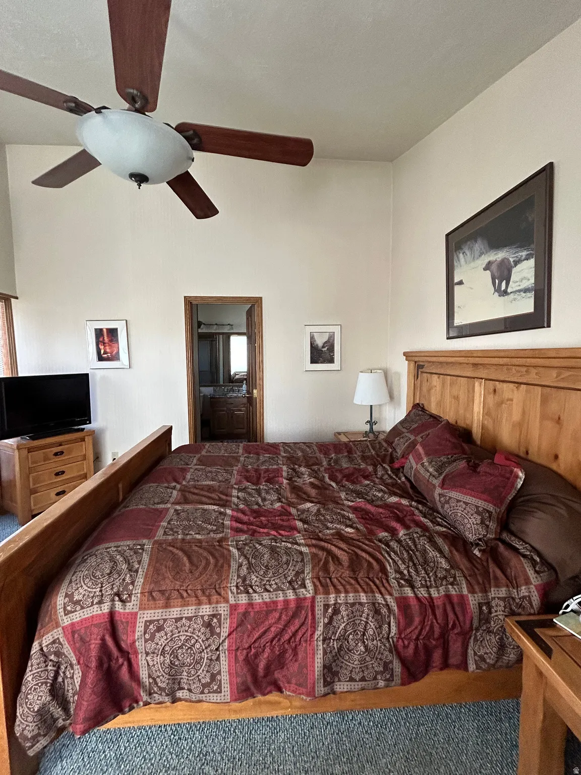 Spacious room featuring a wood-finish ceiling fan, neutral wall tones, and plush carpet flooring