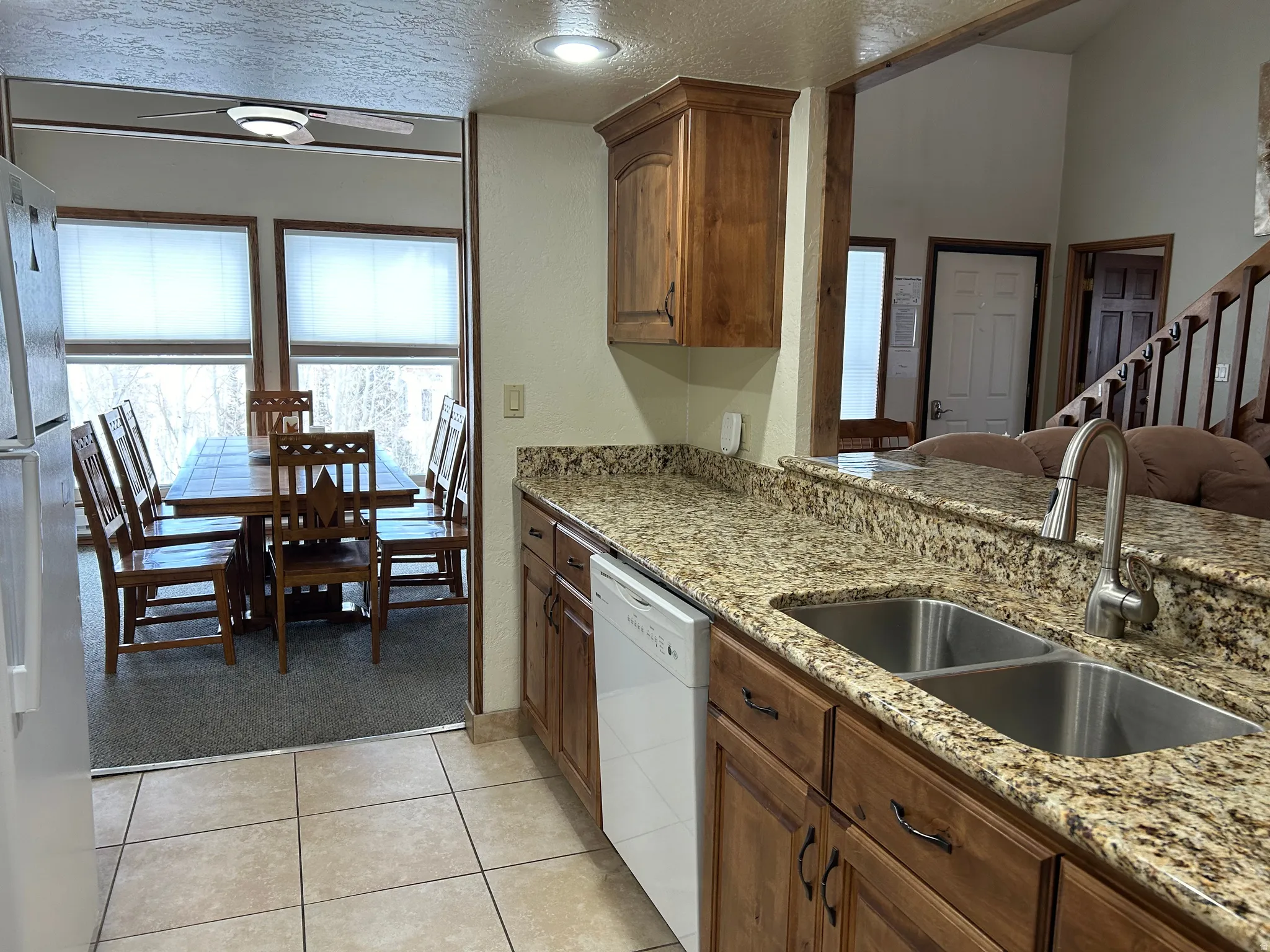 Kitchen with tile flooring, wood cabinetry, stone countertops, and a dual basin stainless steel sink with a gooseneck faucet