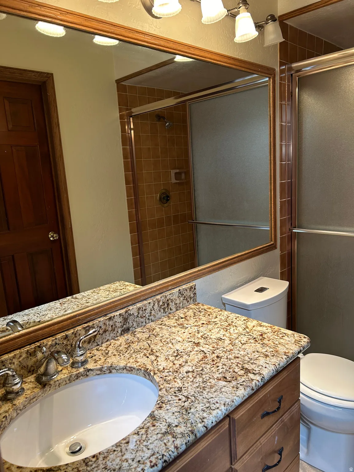 Bathroom featuring a vanity with an oval undermount sink, a stone-finish countertop, and a wood-finish cabinet with dark hardware
