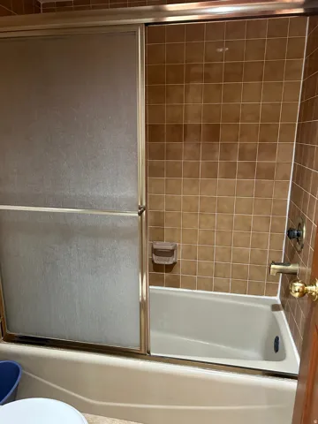 Full bathtub with tiled surround and sliding frosted glass shower doors
