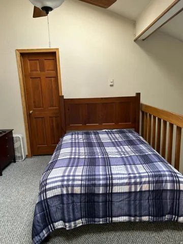 Carpeted bedroom with a natural wood door, wood-finish ceiling fan, and sloped ceiling