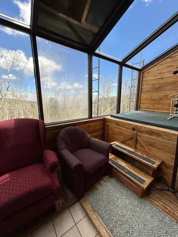 Sunroom featuring sloped glass walls and ceiling, natural wood paneling, and a raised platform with wooden steps