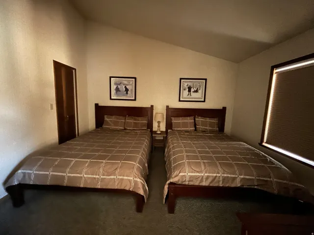 Vaulted ceiling with an angled wall, two dark-wood bed frames, a window with a cellular blind, and dark carpeting