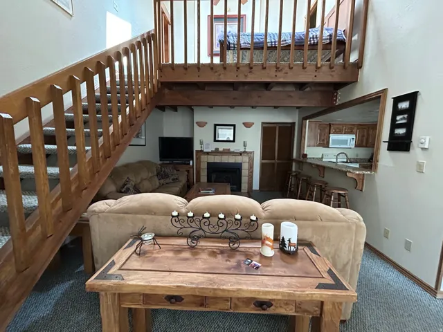 Open-concept living area featuring a wood staircase with carpeted treads, a loft space with a wood railing, and a kitchen pass-through with a breakfast bar