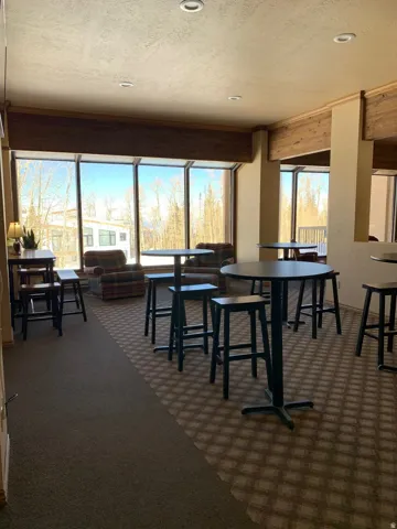 Expansive commercial space featuring large picture windows, recessed lighting, wood-finish ceiling beams, and patterned carpet flooring