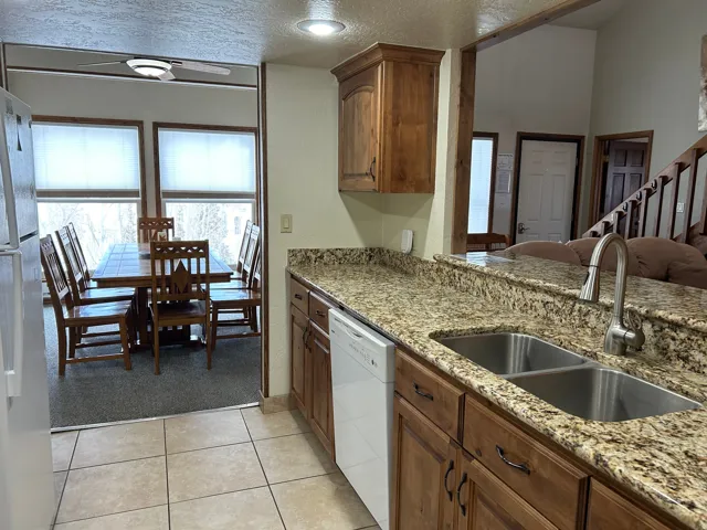 Kitchen with tile flooring, wood cabinetry, stone countertops, and a dual basin stainless steel sink with a gooseneck faucet