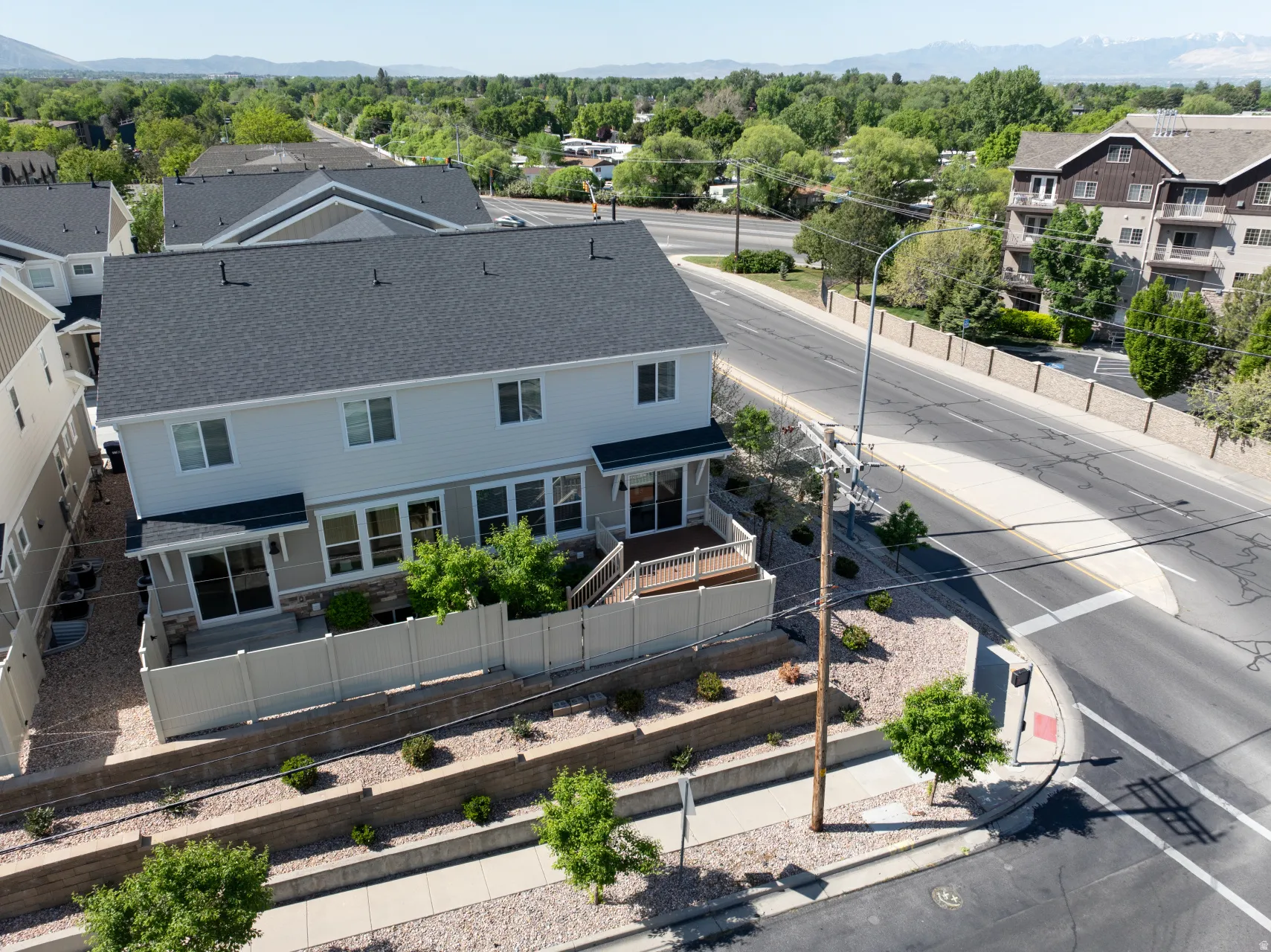 Two-story residence featuring light-toned siding, a dark shingle roof, and a private rear patio with a white fence
