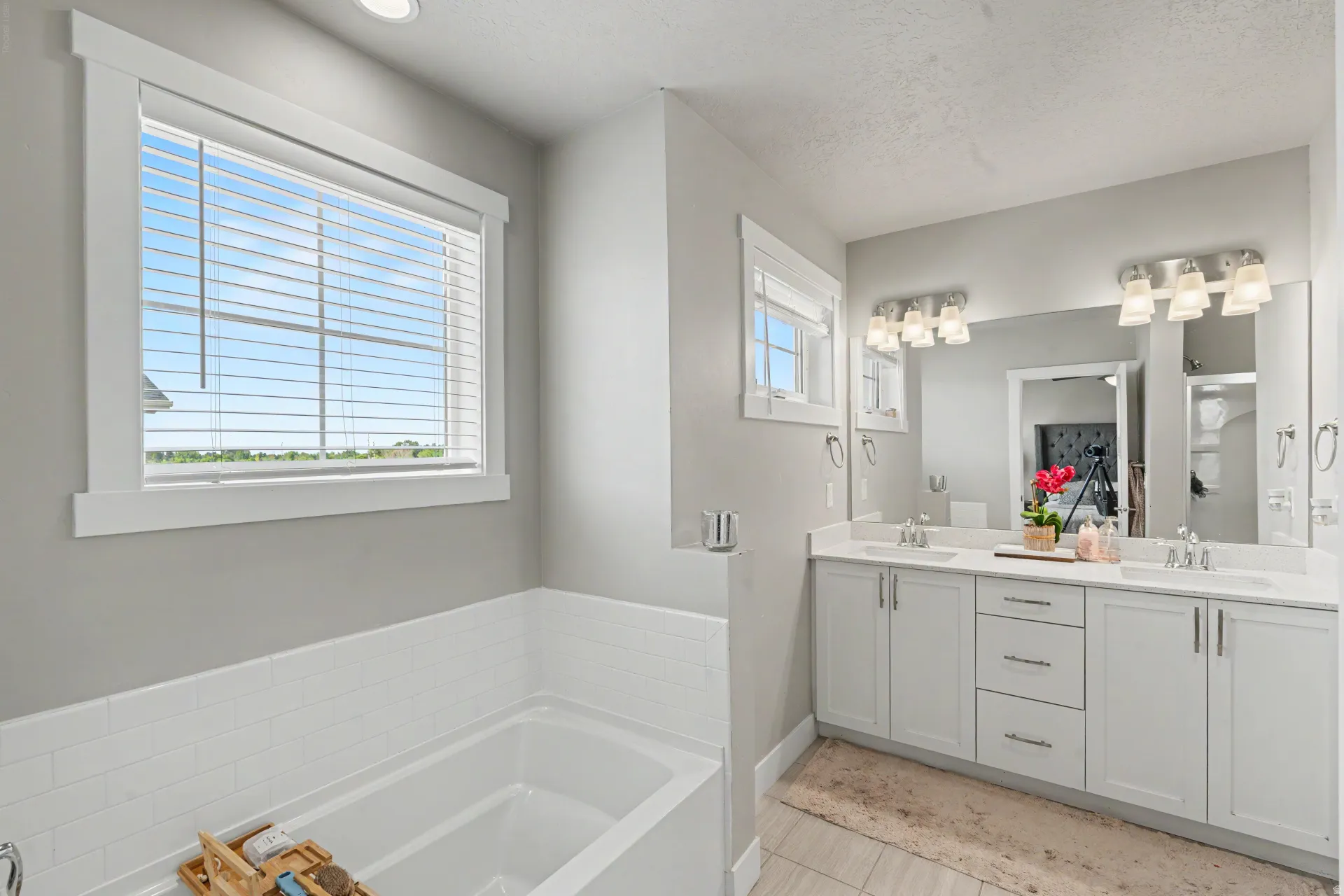 Bathroom featuring a built-in soaking tub with white subway tile surround, a large window with white trim, and a dual-sink vanity with white cabinetry and an expansive mirror