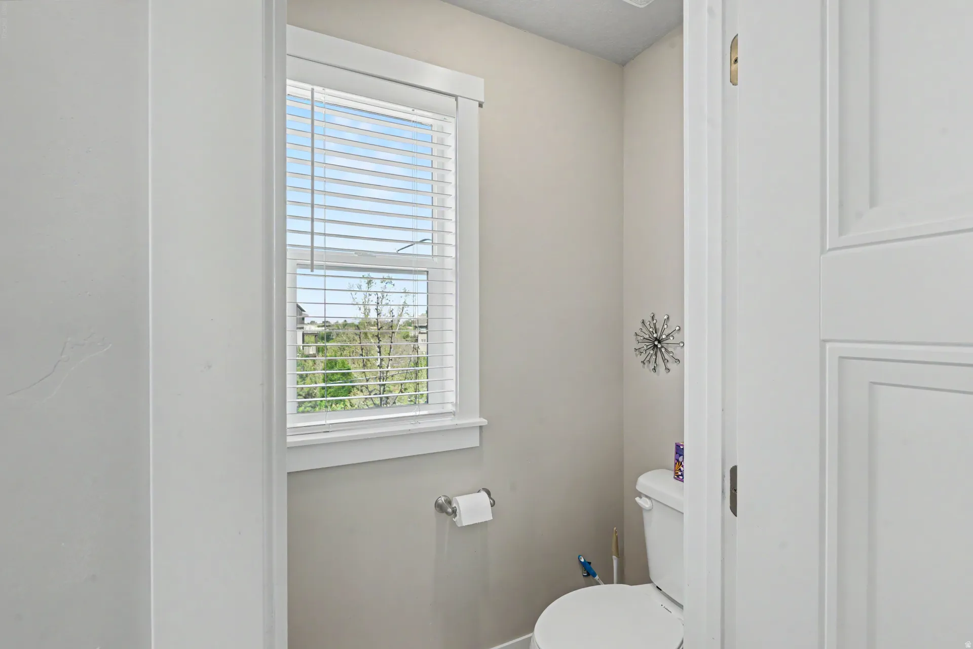 Powder room with a single window featuring horizontal blinds, neutral wall paint, and a white paneled door