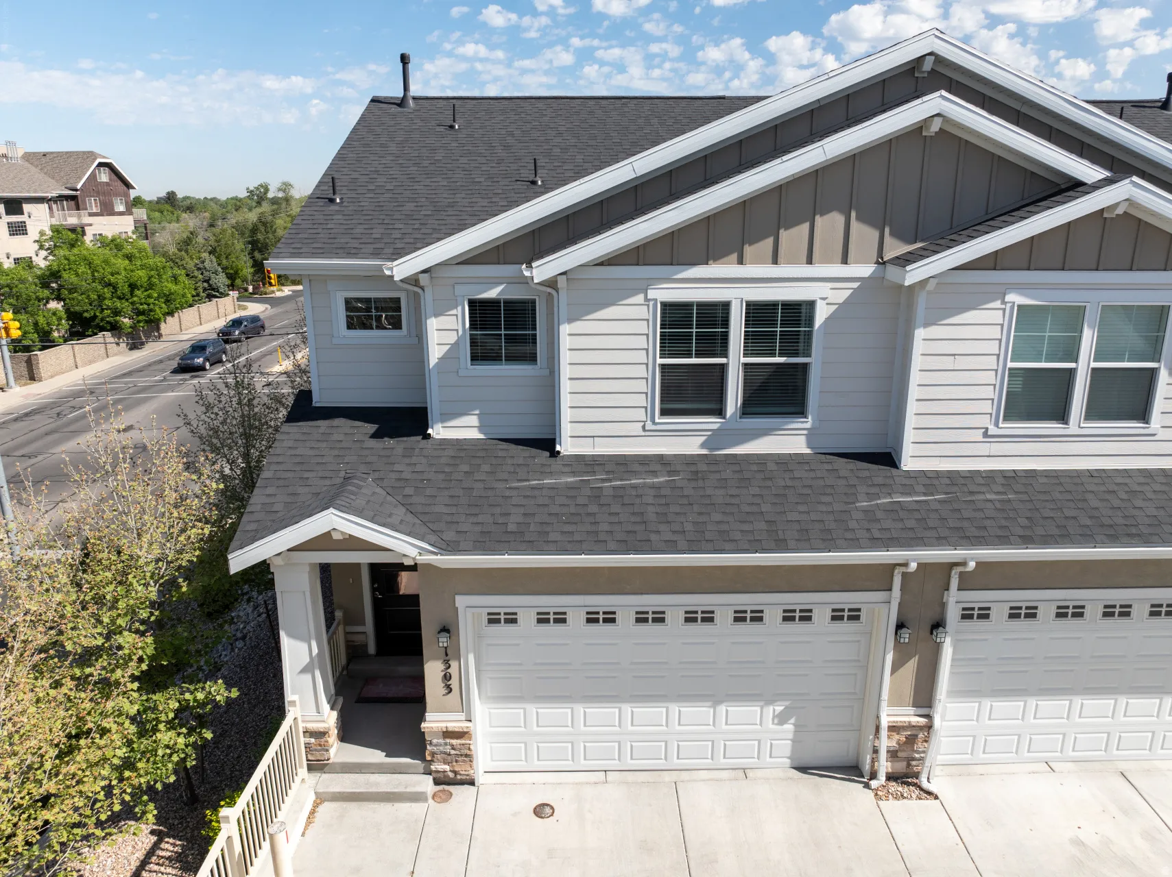 Multi-story residence featuring a two-car garage with panel doors, stone accents, and light-colored siding