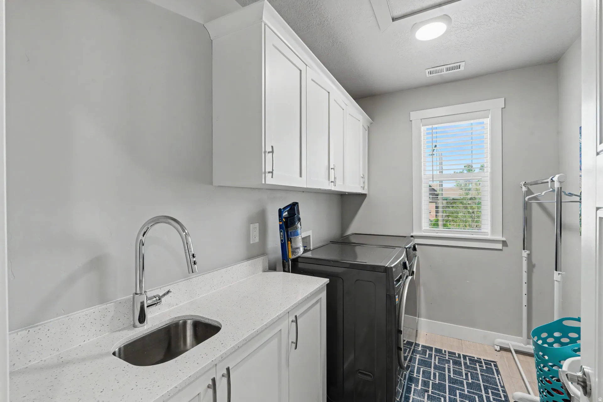 Laundry room featuring white cabinetry, a light-colored countertop with an undermount sink, and a chrome faucet