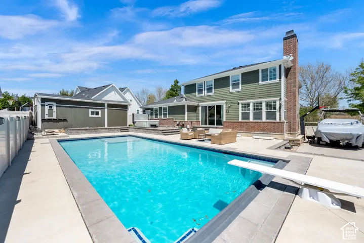Expansive backyard featuring an in-ground swimming pool with a diving board, concrete surround, and a hot tub