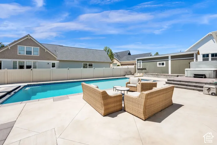 Expansive concrete patio featuring an in-ground swimming pool, a built-in spa, a privacy fence, and an adjacent shed