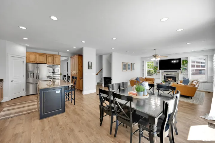 Recessed lighting throughout, LVP wood-finish flooring, built-in shelving, stainless steel appliances, and a fireplace with a stone surround