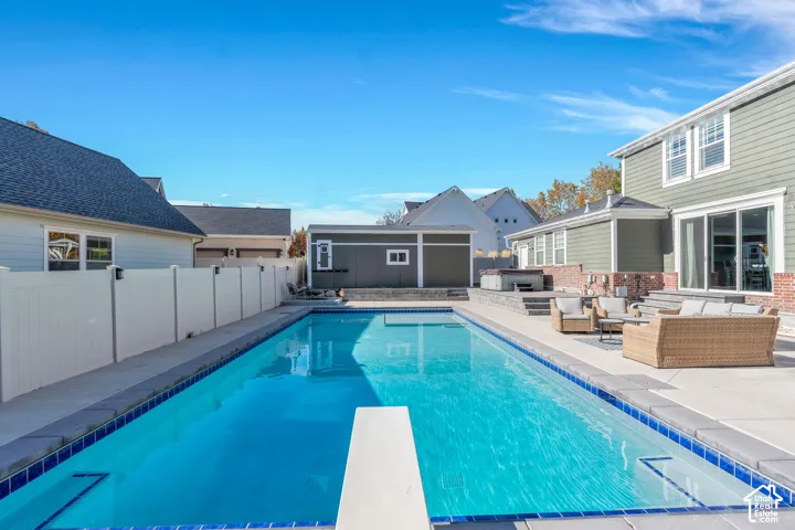 View of pool with diving board, featuring patio surround, a fenced backyard, and an outdoor lounge area