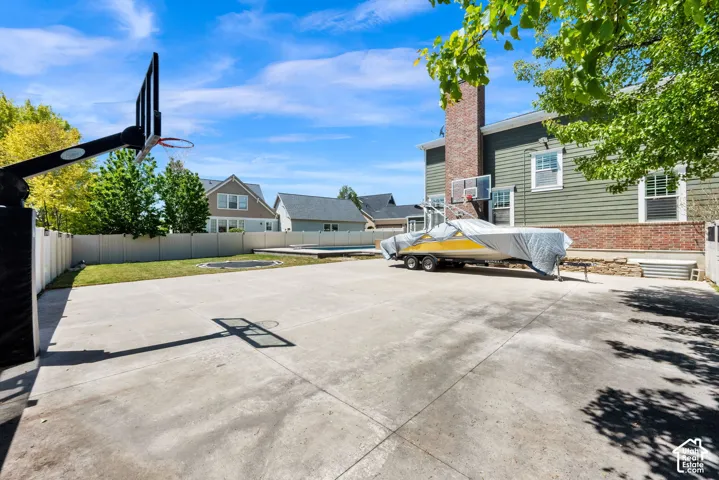 Expansive concrete pad, basketball hoop, pickleball court in a fully fenced yard, and a visible inground pool