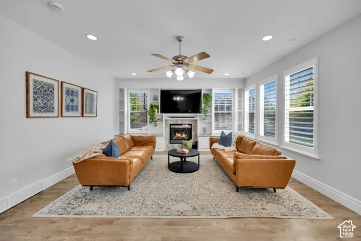 Recessed lighting, LVP wood-finish flooring, built-in shelving, a fireplace with a stone surround, and windows with shutters