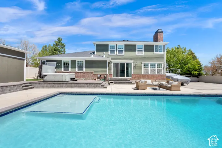 In-ground swimming pool with integrated tanning ledge, expansive concrete patio, and hot tub