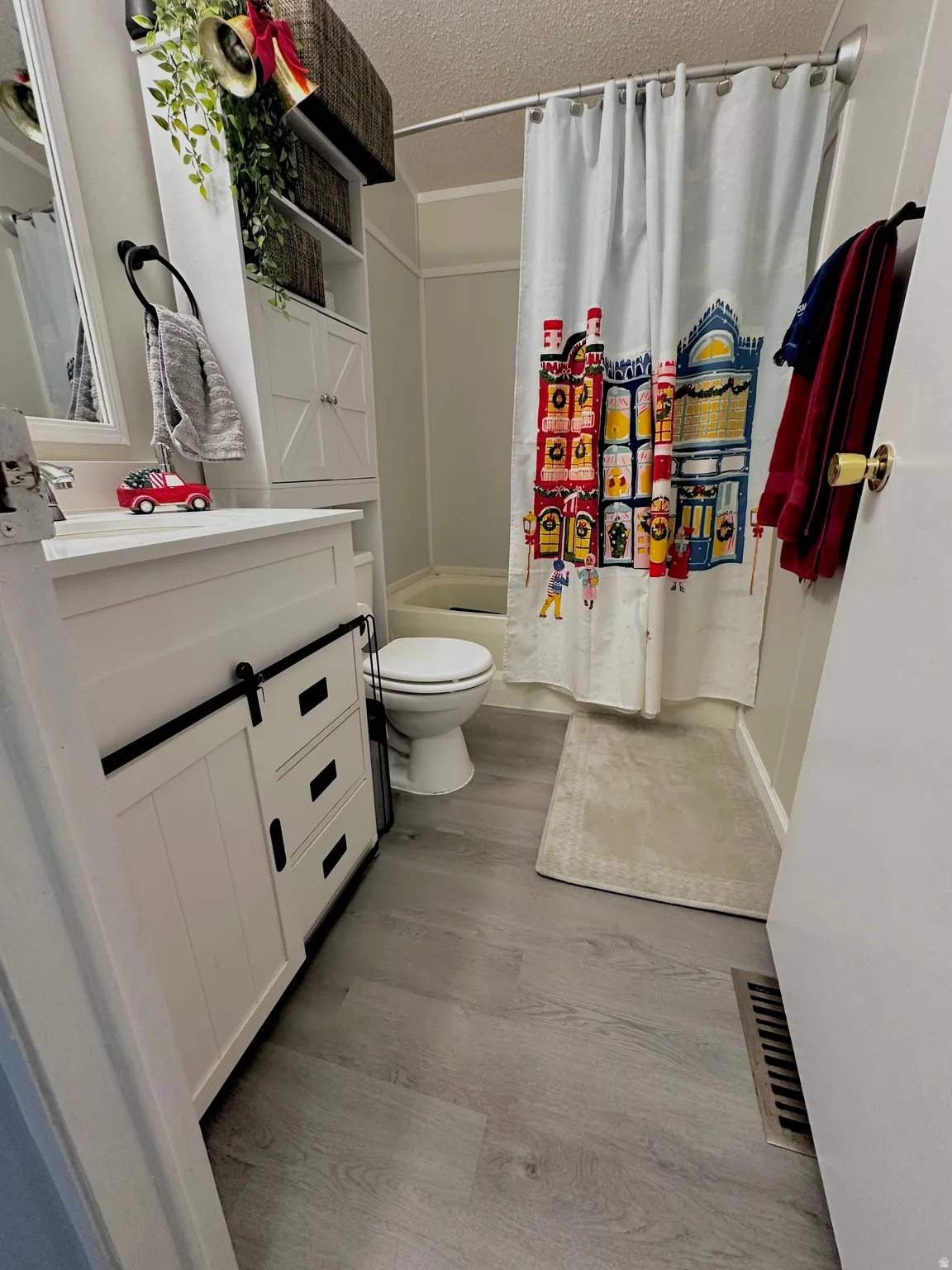 Bathroom featuring a white vanity with barn door style cabinetry, light wood-finish flooring, a white toilet, and a white bathtub with shower