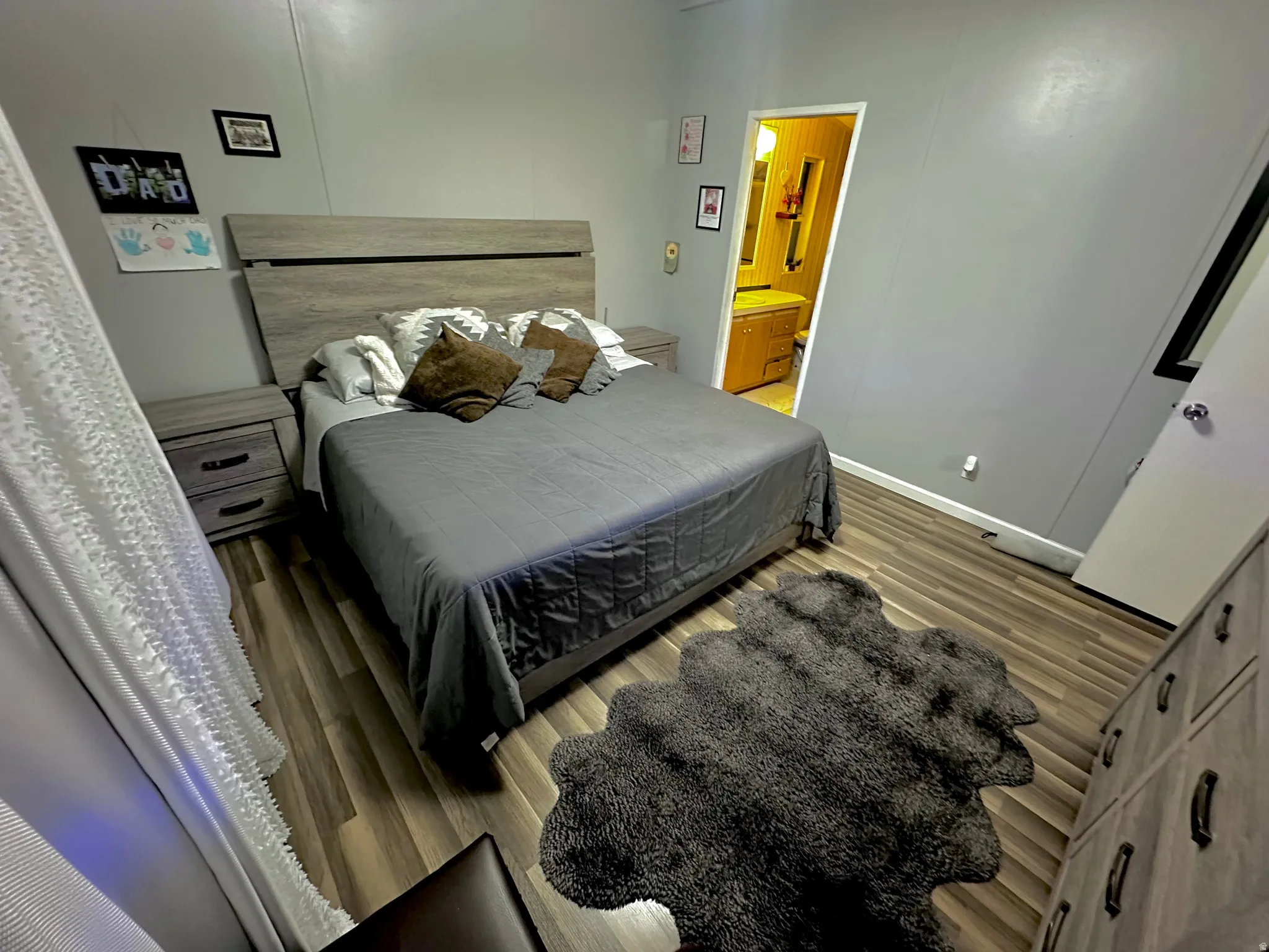 Bedroom featuring wood-finish flooring, light grey walls, and a wood-tone headboard with coordinating nightstands