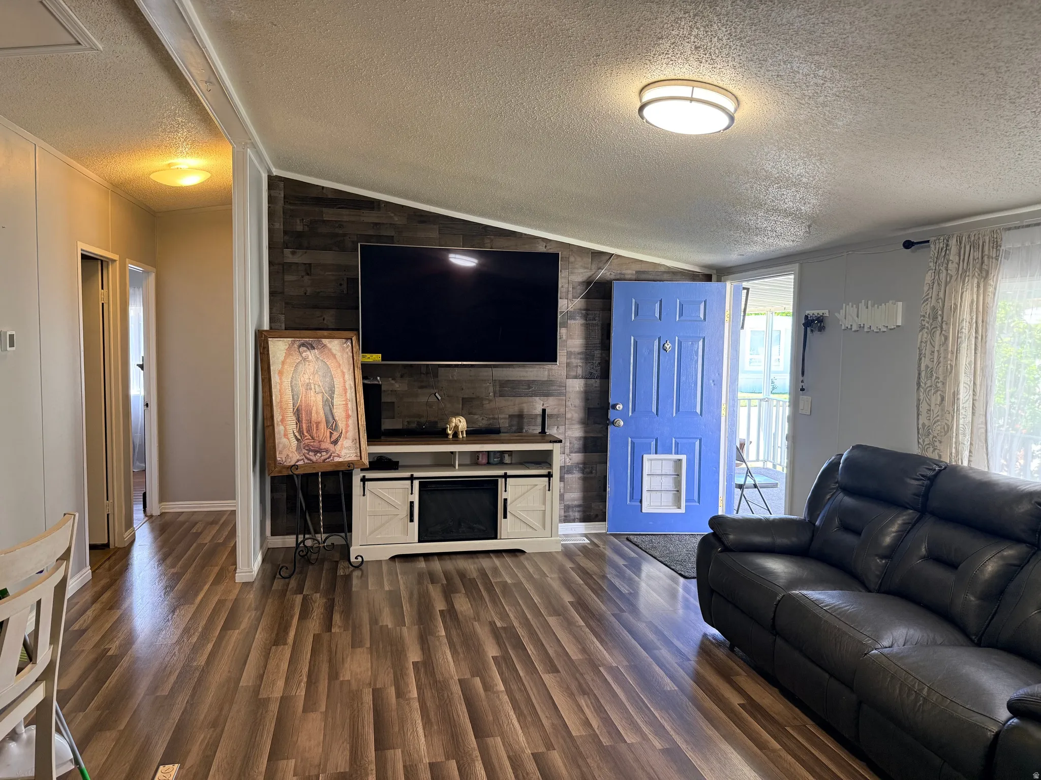 Living area featuring wood-finish flooring, a decorative accent wall with horizontal wood planks, and a blue entry door
