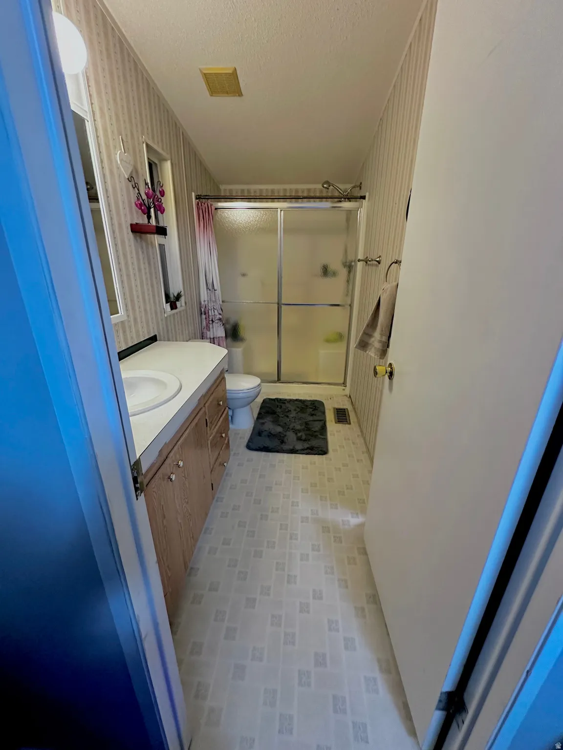 Bathroom featuring a wood-finish vanity with an integrated sink, a white toilet, and a shower with sliding glass doors