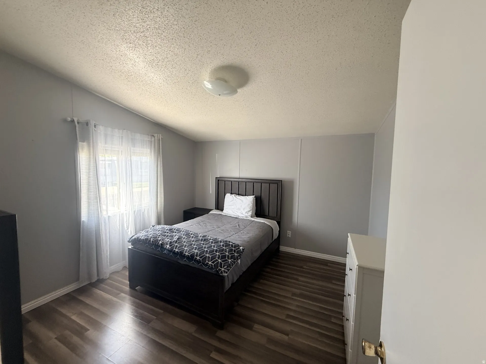 Spacious room featuring wood-finish flooring, a contemporary ceiling light fixture, and a window with sheer curtains
