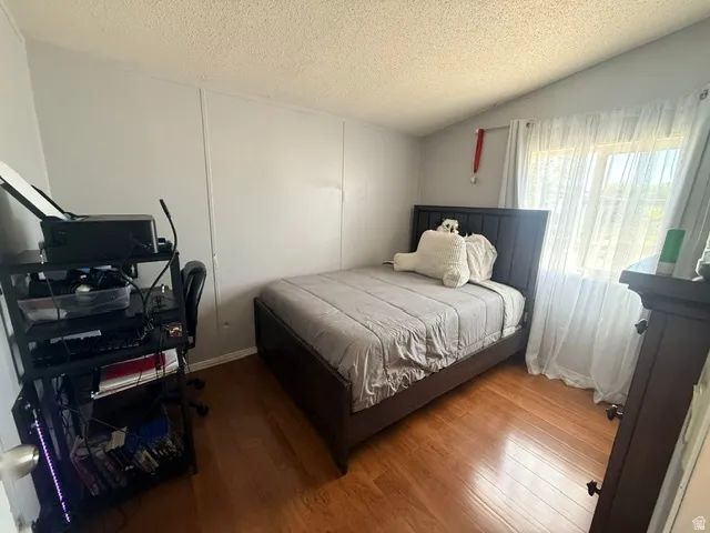 Bedroom featuring wood-finish flooring, a window with sheer curtains, and light-colored walls