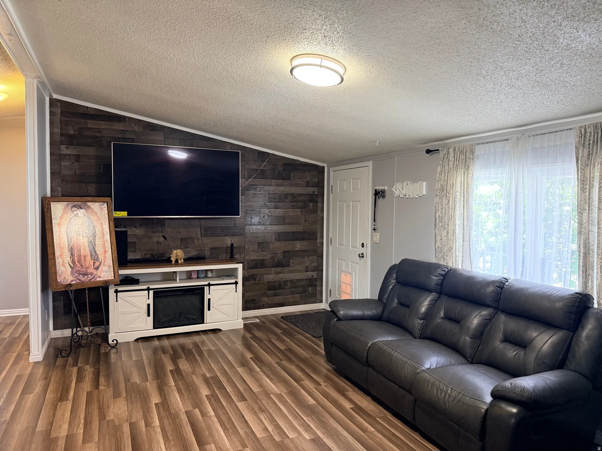 Living area featuring wood-finish flooring, a decorative accent wall with horizontal wood paneling, and a white paneled entry door