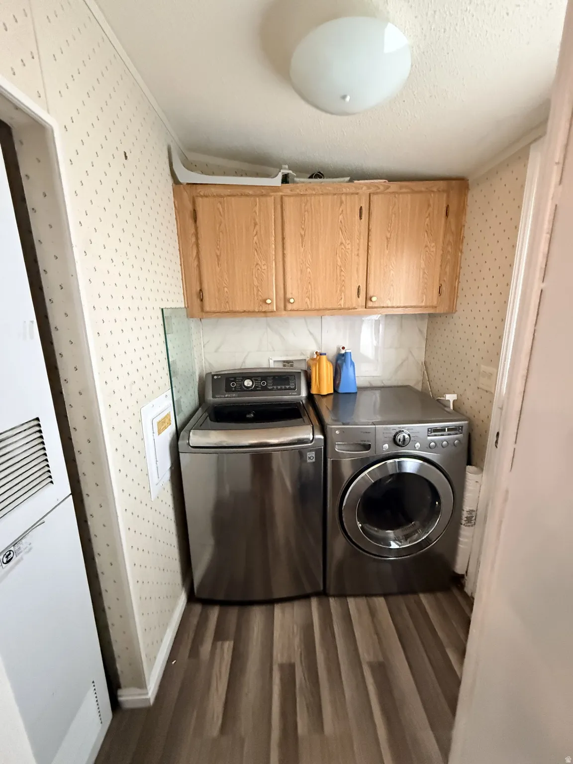Dedicated laundry area featuring wood-finish flooring, overhead cabinetry, and a ceiling-mounted light fixture