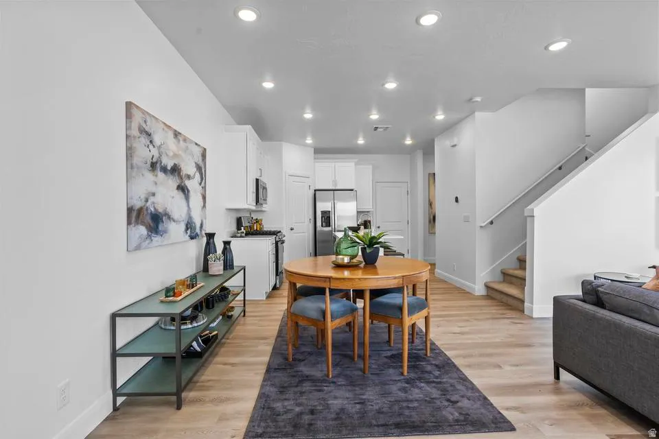 Open-concept living space featuring wood-finish flooring, recessed lighting, white walls, and a staircase with a white handrail