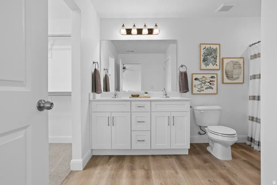 Dual sink vanity with white cabinetry, a large mirror, and overhead lighting