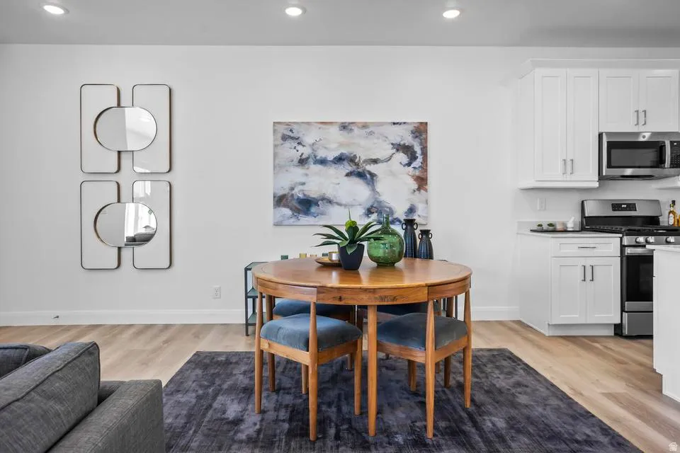 Bright open-concept living area featuring light wood-finish flooring, recessed lighting, and a kitchen with white shaker cabinetry, stainless steel appliances, and a tiled backsplash