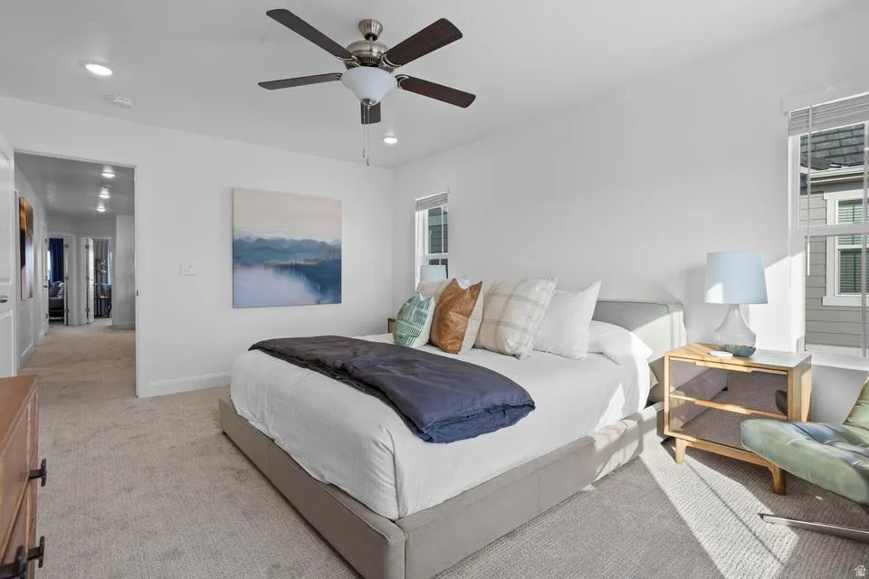 Spacious bedroom featuring light neutral carpet, white walls, and a contemporary ceiling fan with integrated lighting