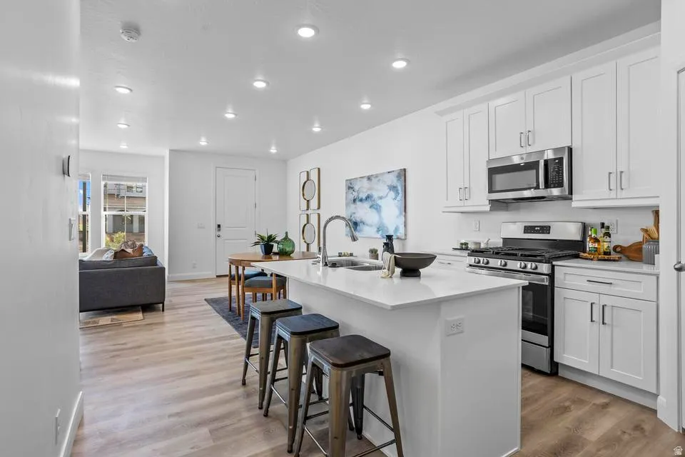 Open-concept kitchen featuring an island with seating, white shaker cabinetry, stainless steel appliances, and wood-finish flooring