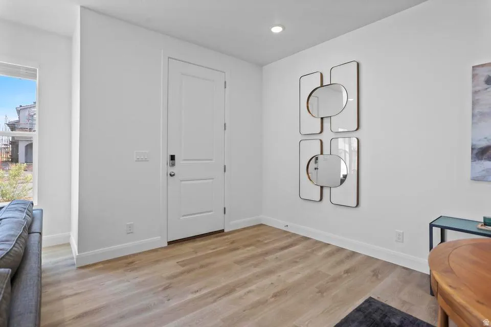 Bright entry area featuring a two-panel white door with dark hardware, recessed ceiling lighting, and light wood-finish flooring