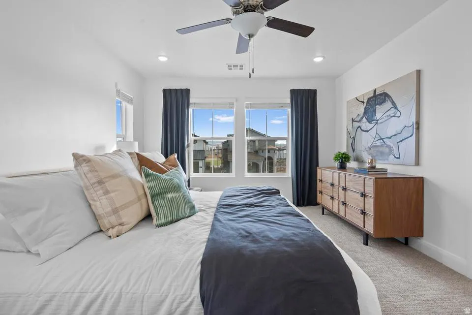 Bright bedroom featuring two windows with dark drapery, recessed lighting, a ceiling fan, and neutral carpeting
