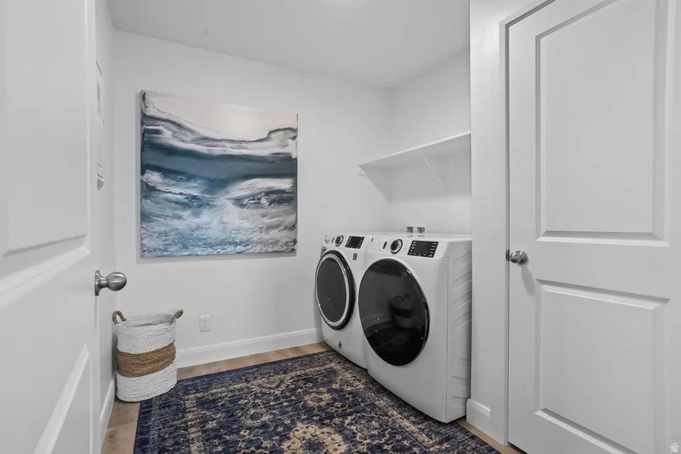 Dedicated laundry area featuring a front-loading washer and dryer, wood-finish flooring, and a built-in wall shelf
