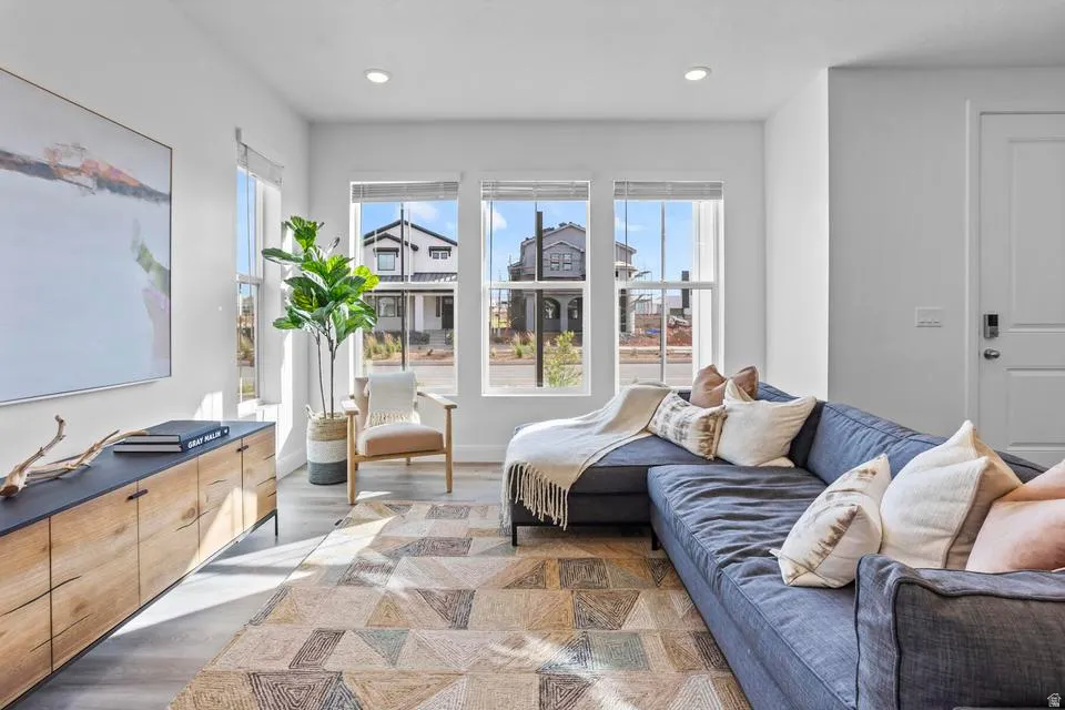 Living area with ample natural light, featuring wood-finish flooring, recessed lighting, and a console with wood-paneled doors