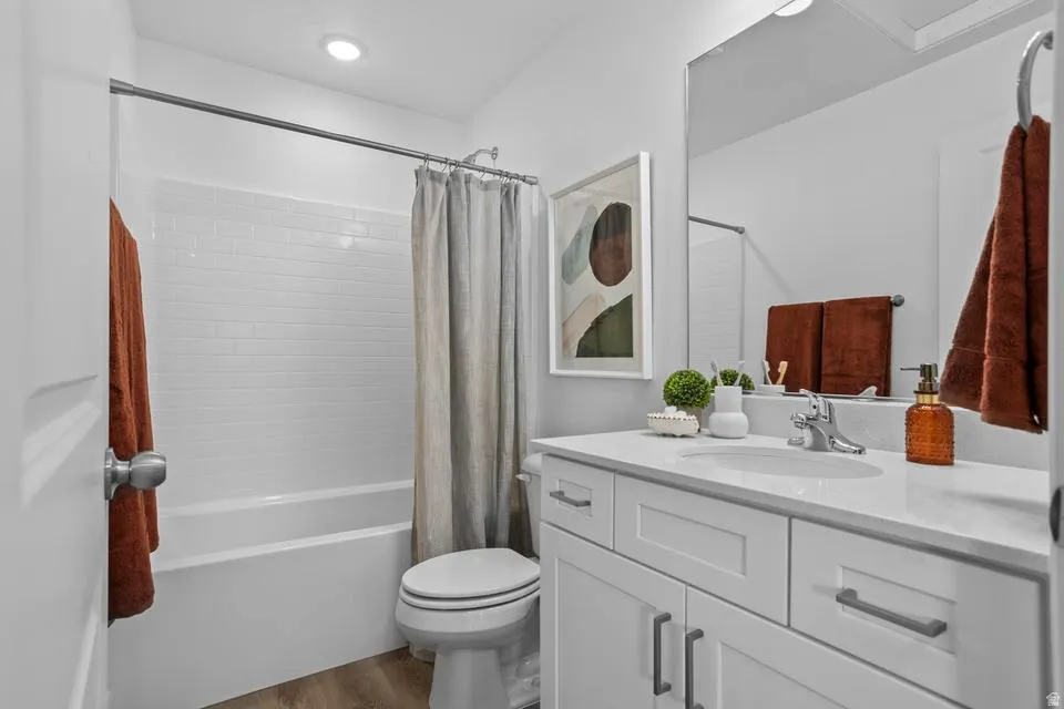 Bathroom featuring a white subway tile shower surround, a white vanity with a light-toned countertop, and wood-finish flooring