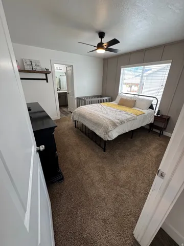 Carpeted bedroom featuring a ceiling fan with integrated lighting, a window with blinds, and panel accent wall