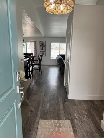 Inviting entryway featuring a light blue door with brushed nickel hardware, wood-finish flooring, a decorative woven ceiling light fixture, and an open layout to interior spaces